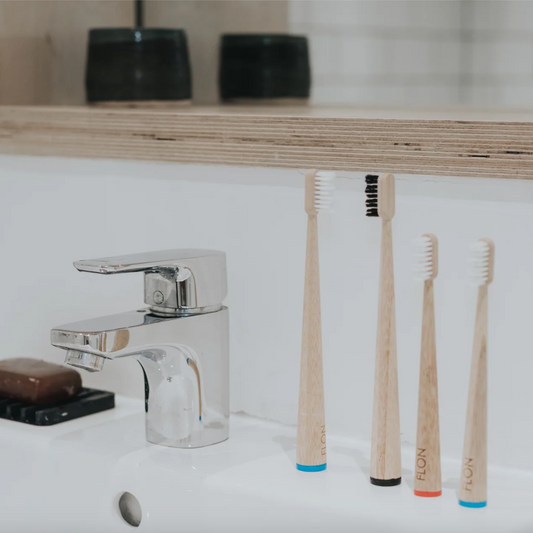 Four FLON bamboo toothbrushes sitting on a sink.