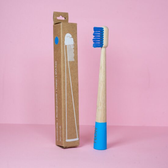 A blue Kids Bamboo Toothbrush next to a box on a pink background for the FLON brand.