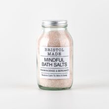 photo of a clear glass jar filled with pale pink bath salts, jar has a white label with black text showing the essential oils in the salts