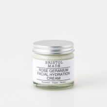 A 60ml clear glass jar of Bristolmade rose geranium face cream, featuring a white label with black text, highlighting its vegan ingredients.