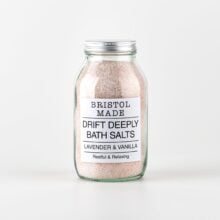 Photo of a 500ml clear glass jar filled with pale pink bath salts, with a white label with black text detailing the product name and how it can help.