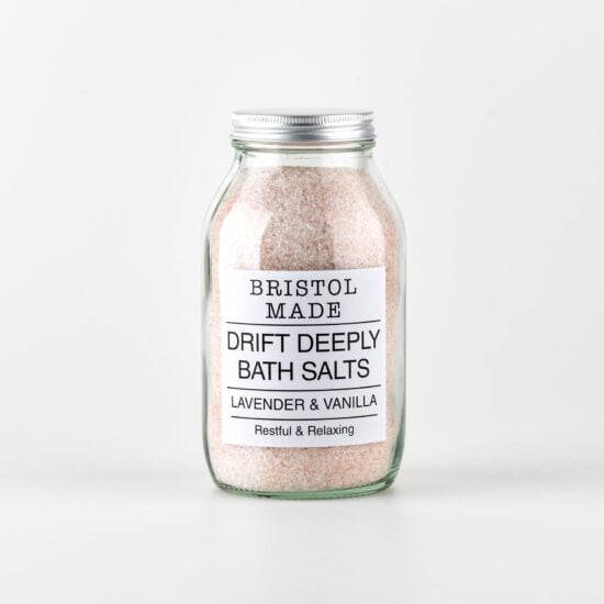 Photo of a 500ml clear glass jar filled with pale pink bath salts, with a white label with black text detailing the product name and how it can help.