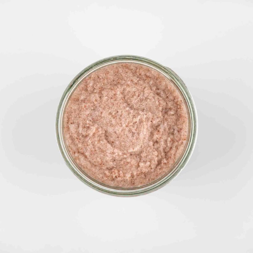 top view of a pale pinky body scrub, showing the exfoliating texture of the salt in the scrub.