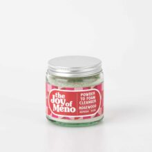 photo of a 120ml clear glass jar, containing a pale green powder cleanser, with a pink patterned label with white text.