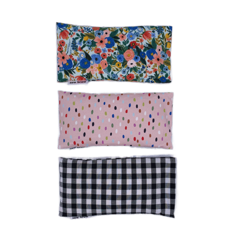 Photo of three lavender eye pillows, one floral, a pink with various coloured spots and a black and white check, on a white background