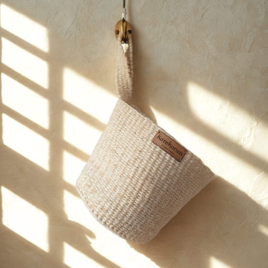 natural Handwoven sisal hanging baskets with twist handles - hanging on brass hooks in soft daylight.