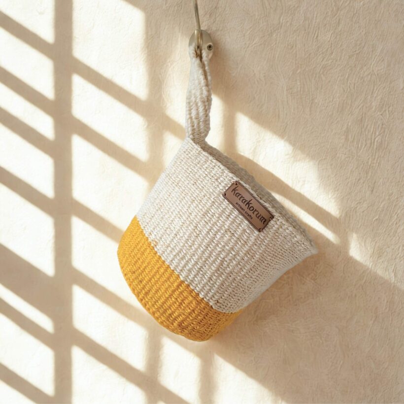 Hanging baskets_Karakorum (3) natural Handwoven sisal hanging baskets with block of mustard colour at the base with twist handles - hanging on brass hooks in soft daylight.