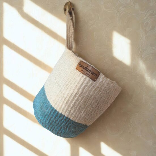 natural Handwoven sisal hanging baskets with block of indigo colour at the base with twist handles - hanging on brass hooks in soft daylight.