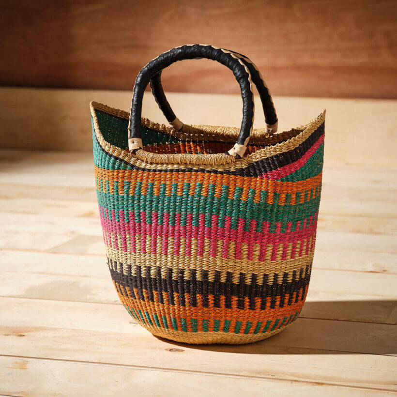 Ethically made woven grass market basket featuring teal, pink, orange and black ladder-stripe bands with leather-wrapped handles.