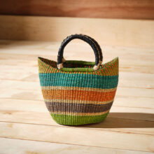 Ethically made woven grass market basket featuring teal, pink, orange and green stripes with leather-wrapped handles.