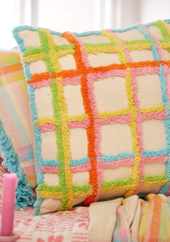 Close up of Handmade tufted check cushion cover in multicolour on a natural recycled cotton base, with tufted grid pattern in orange, pink, yellow, green and blue, finished with a blue tufted border. 45x45cm.