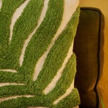 Close up detail of Hand tufted palm leaf cushion cover in green on a natural recycled cotton base, with a large frond design in tufted pile. 45x45cm, handmade in India.