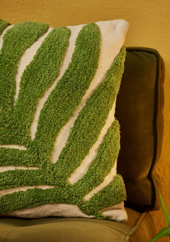 Close up detail of Hand tufted palm leaf cushion cover in green on a natural recycled cotton base, with a large frond design in tufted pile. 45x45cm, handmade in India.